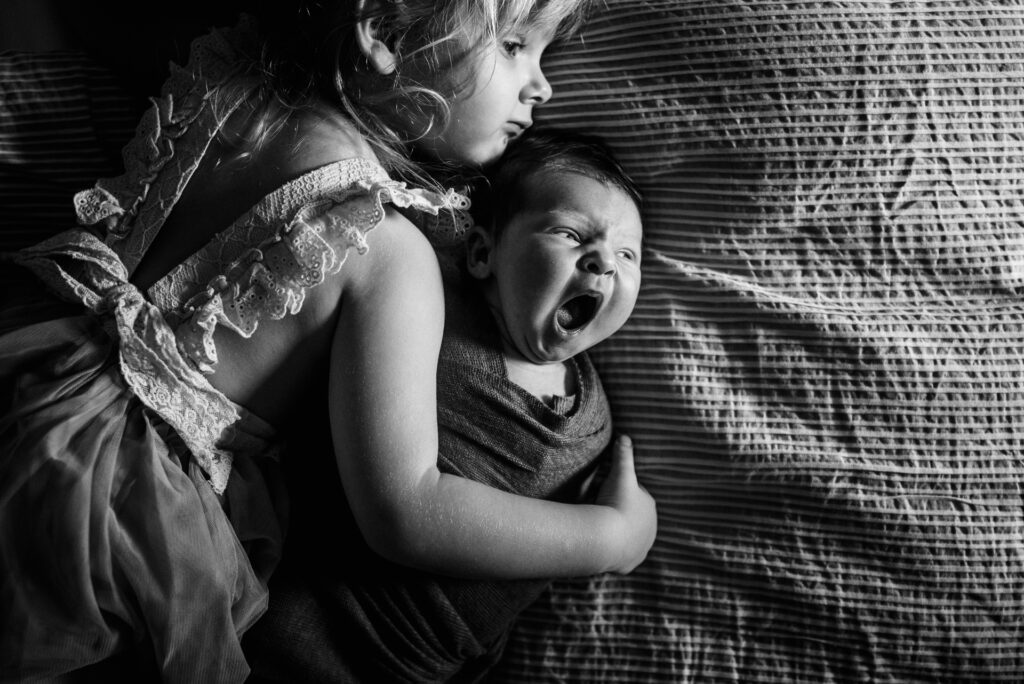 Little sister hugging her newborn brother as their lay on mom and dad bed during Jacksonville newborn session