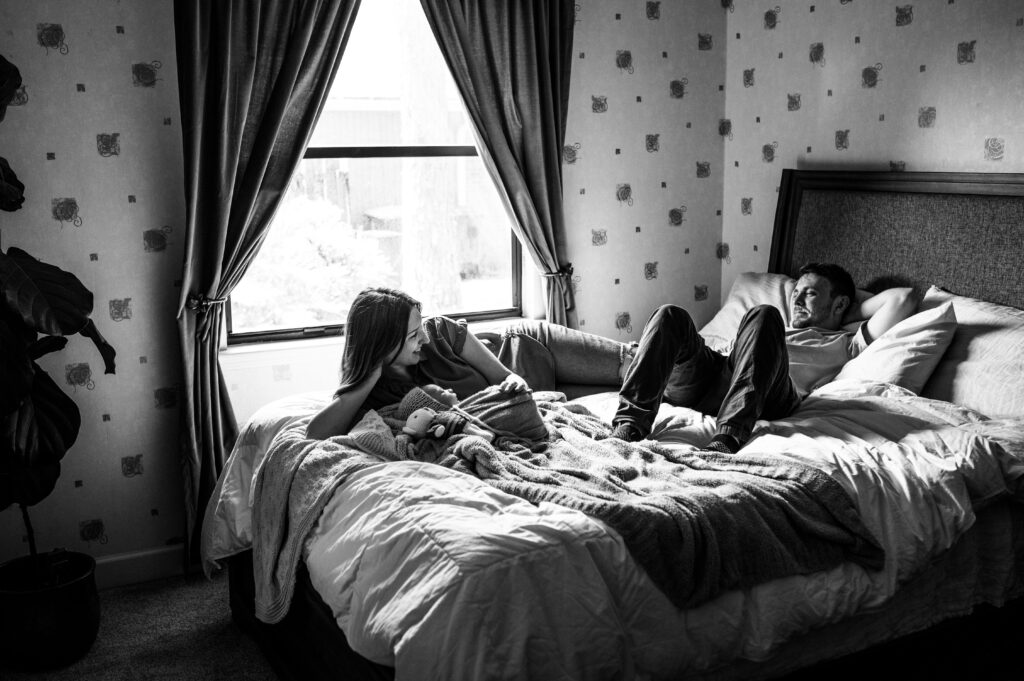 Cozy moment from at home newborn session of parent laying in the bed with their baby by Jacksonville newborn photographer
