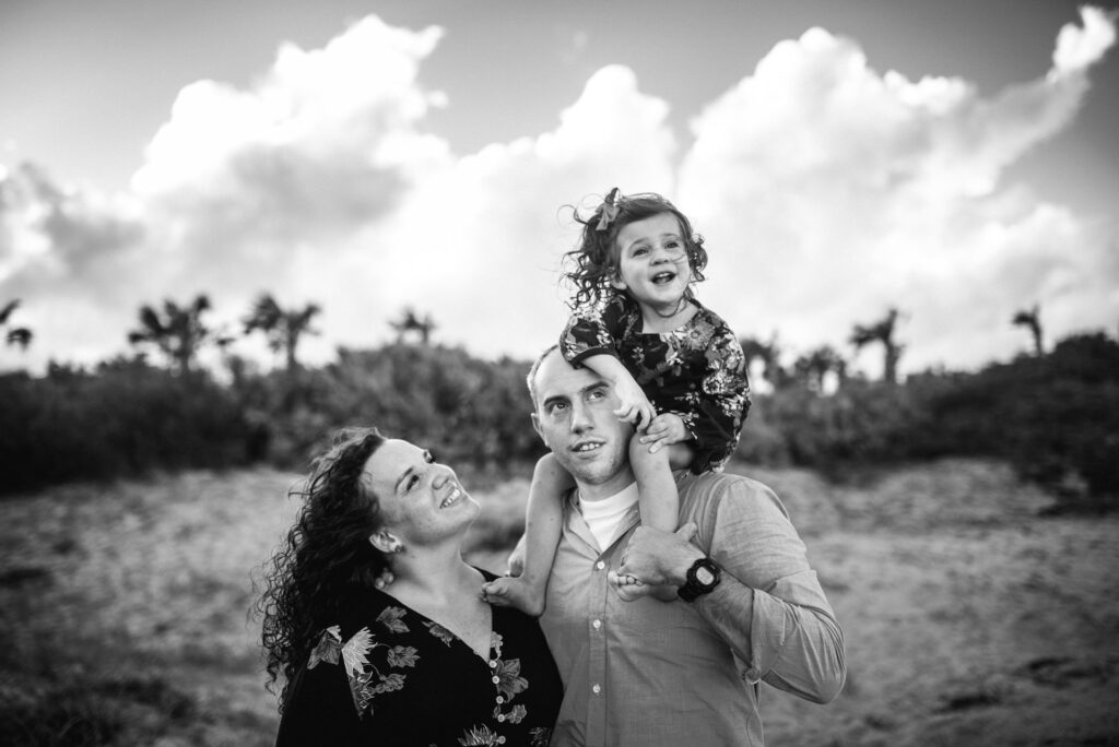 Parents posing for a photo with small child sitting on father's shoulders in a family photoshoot in Jacksonville FL