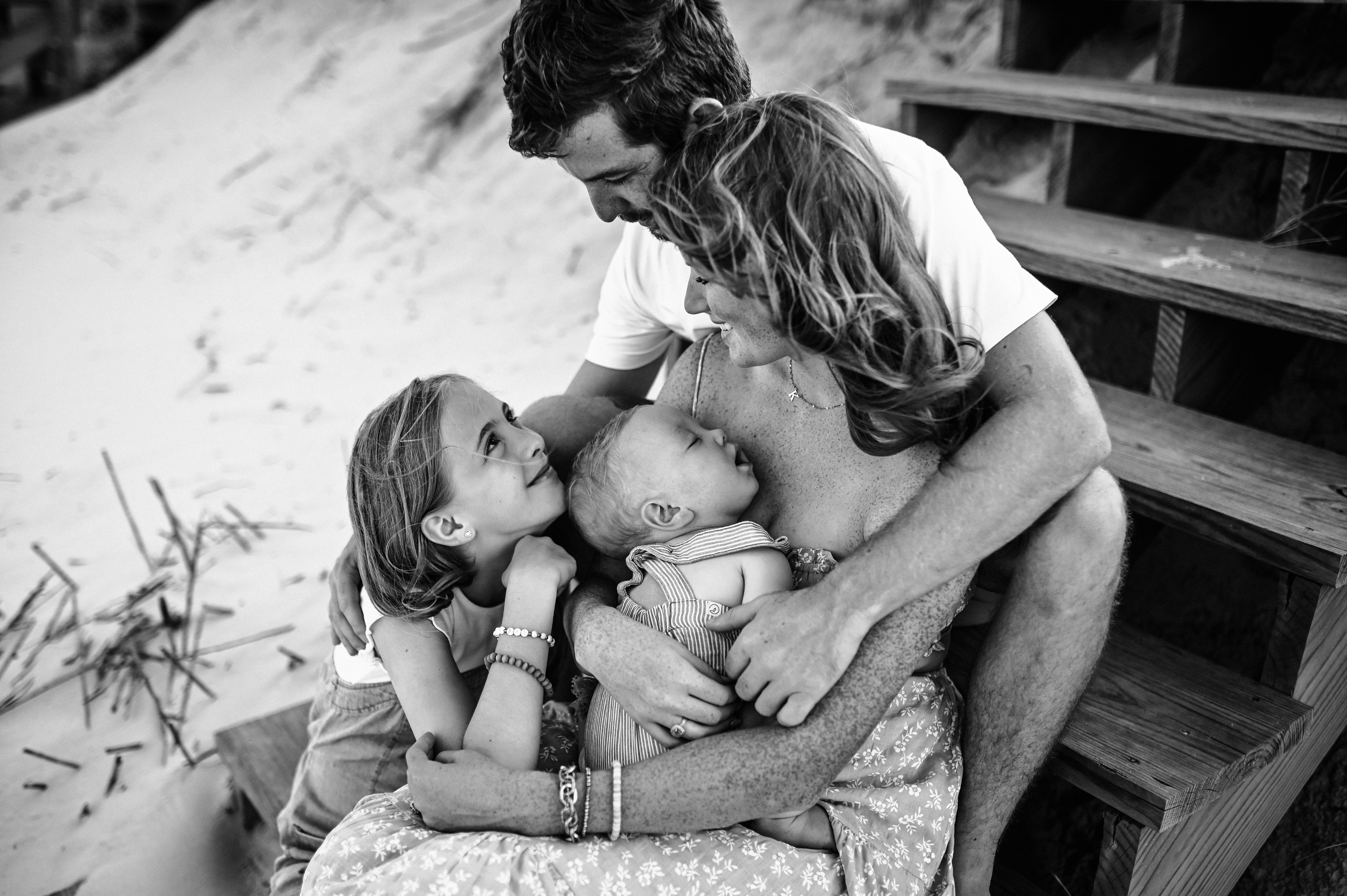 Sweet moment of snuggles with big sister and little baby and their parents sitting on the sand in the Jacksonville Beach