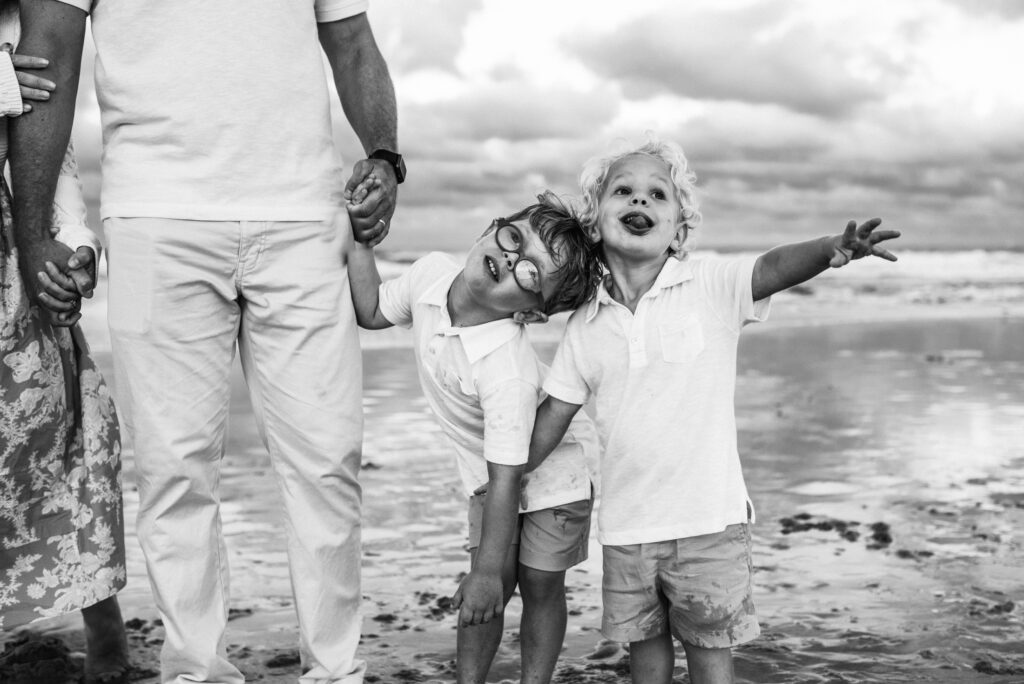 Two silly boys goofing around holding hands with their parents during their family photos on Jacksonville beach