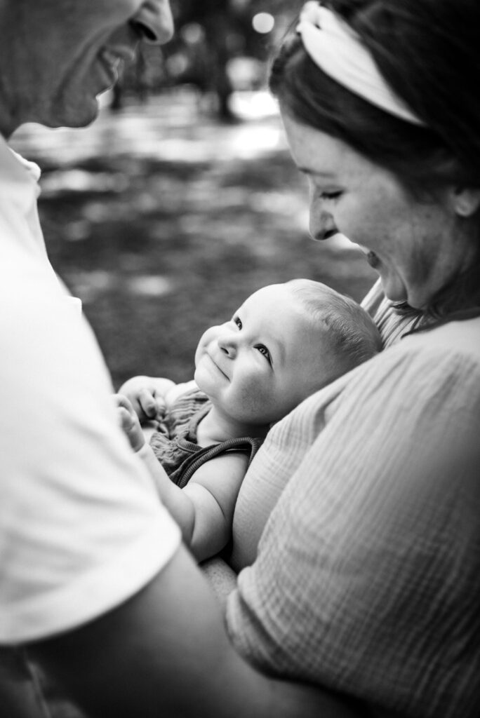 Black and white photo of baby looking up at his parents with adoration during family session in the park by Jacksonville family photographer