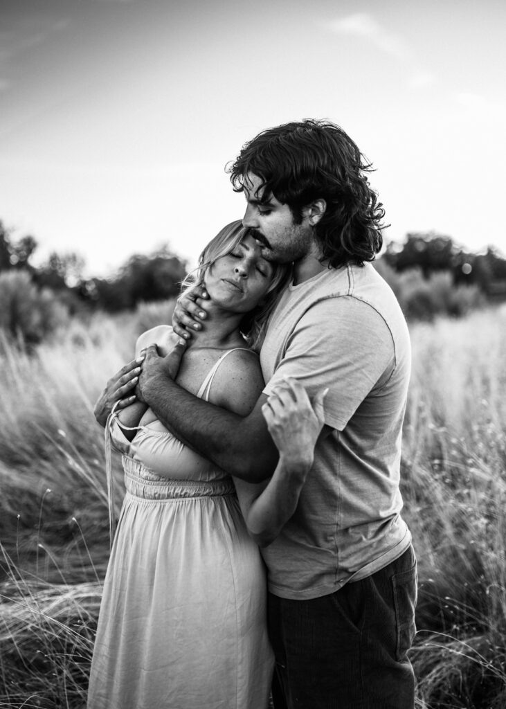 Emotive black and white portrait of a couple embracing in a grassy field at sunset, captured by a Jacksonville engagement photographer