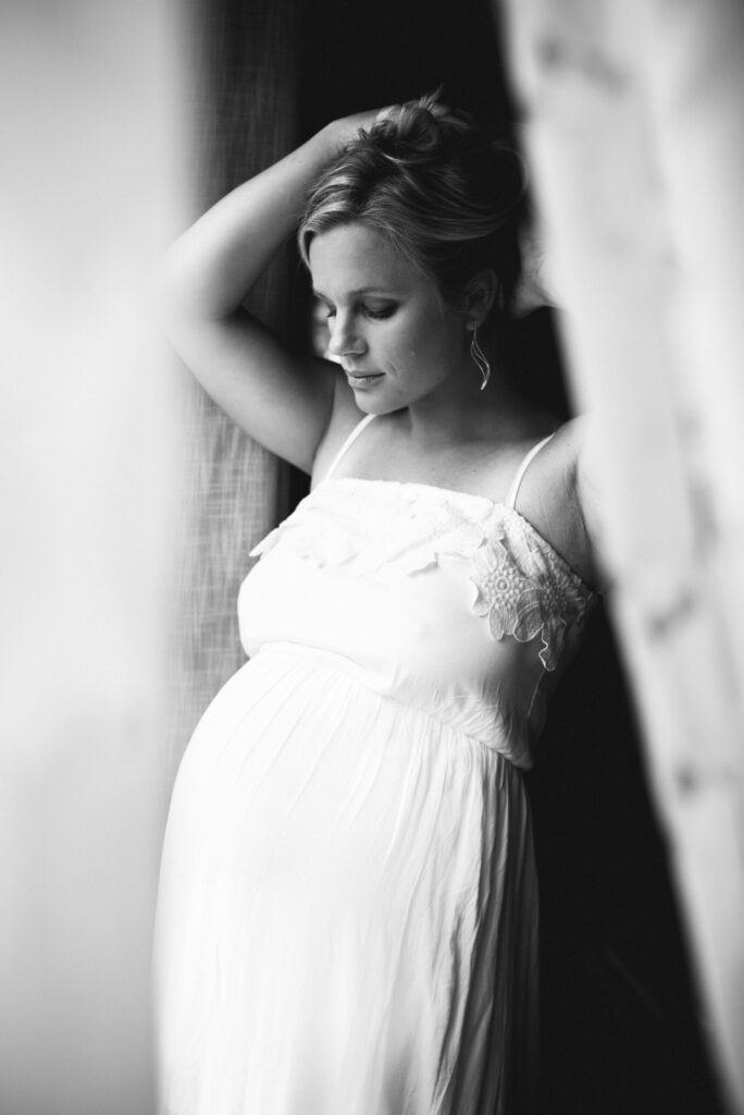 at home portrait of mom to be fixing her hair by the window by Jacksonville pregnancy photographer
