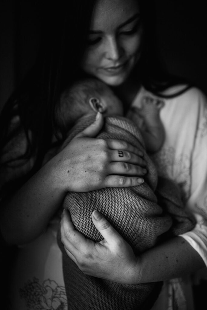 emotive black and white portrait of mom holding a baby in the deep shadows of the window by Jacksonville newborn photographer