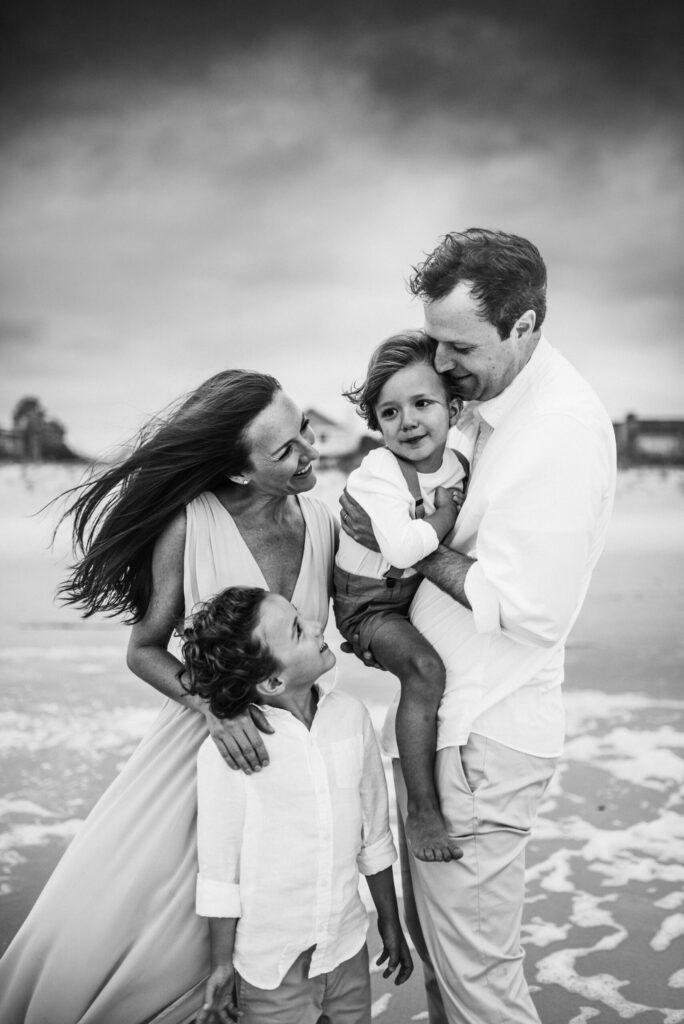 Black and white family portrait during windy family session of two kids being surrounded by their parents