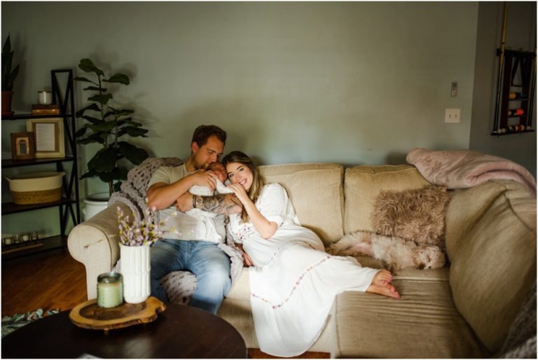 lifestyle icapture of parents resting on their couch with their newborn baby on the livivng room couch, snuggling togeter in the beautiful light captured by Jacksonville newborn photographer Monika Colichio