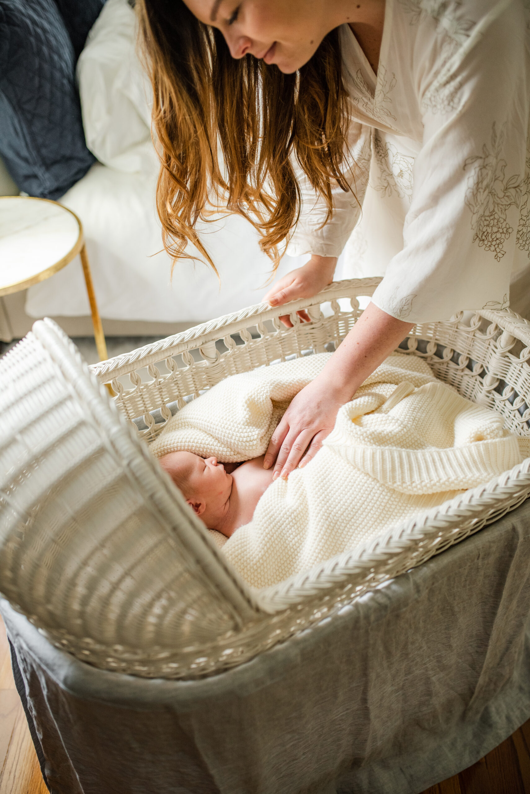 Sweet portrait of momma fixing her baby in the wicker bassinet as window light shines upon them captured by Jacksonville lifestyle newborn photographer