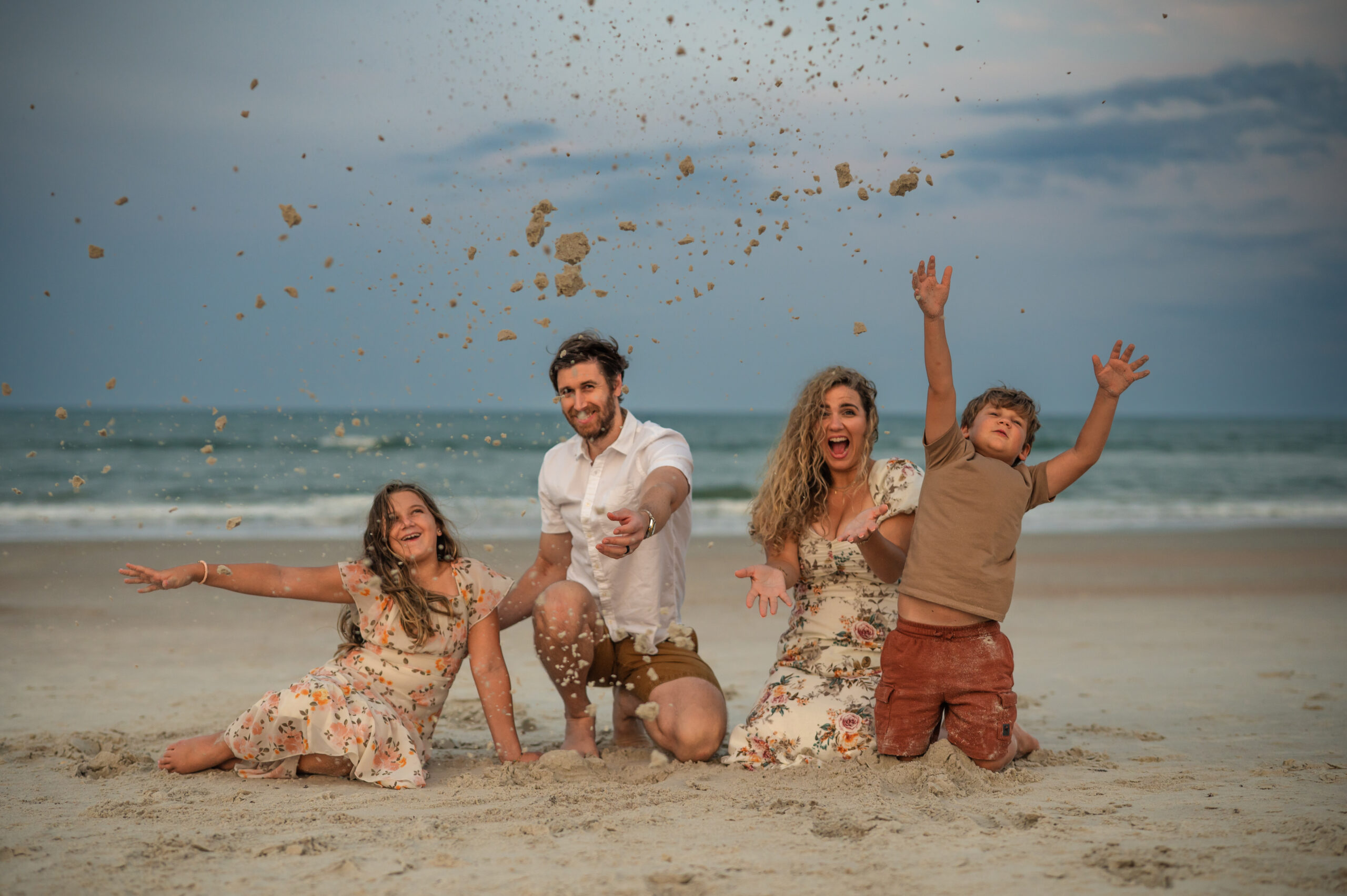 family of four throwing sand in the air as their laugh and having fun during sunset beach session at Ponte Vedra Beach with Jacksonville emotive family photographer