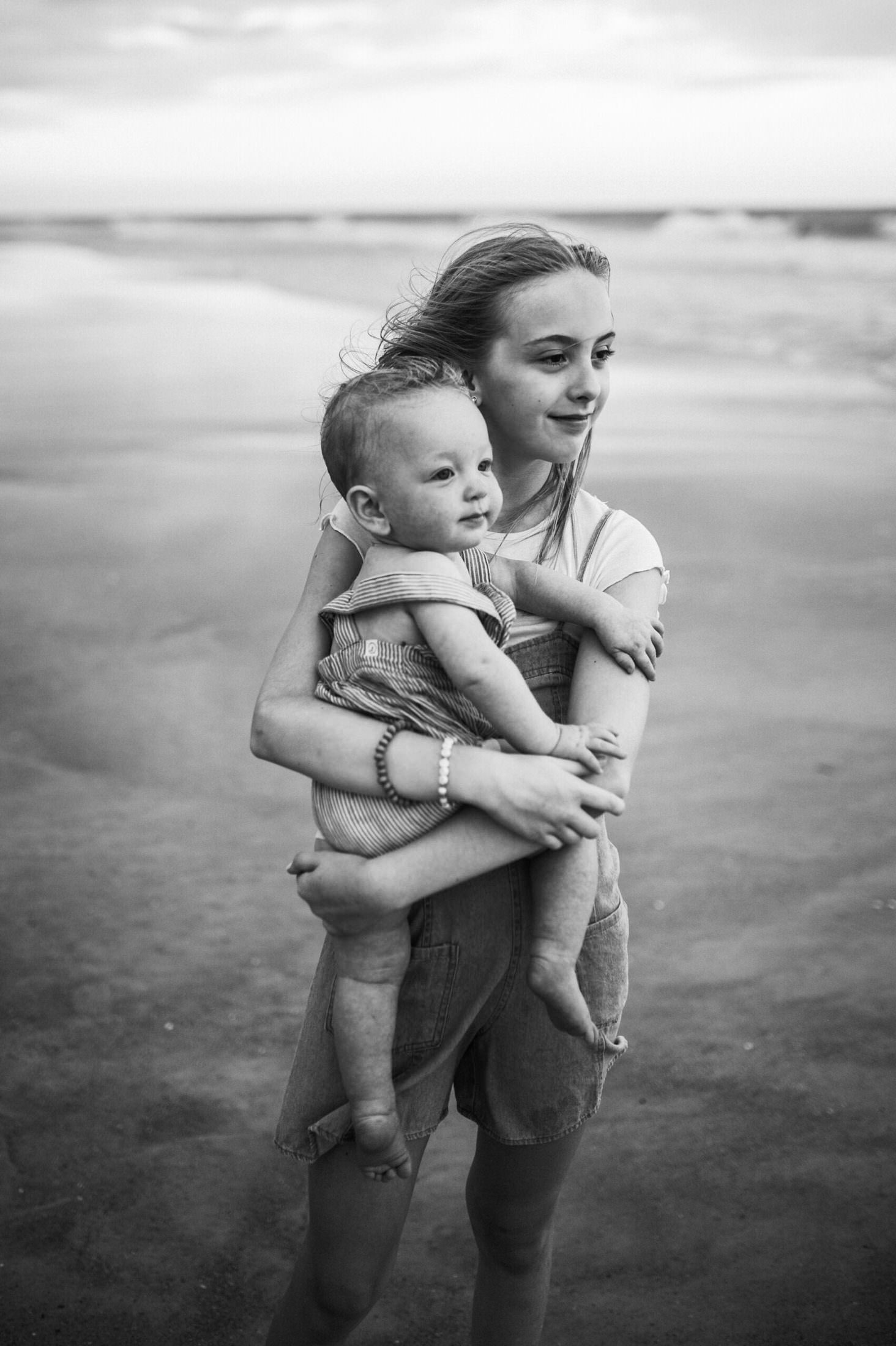 child holding a baby in the beach shore for a photo in a Jacksonville children's photoshoot