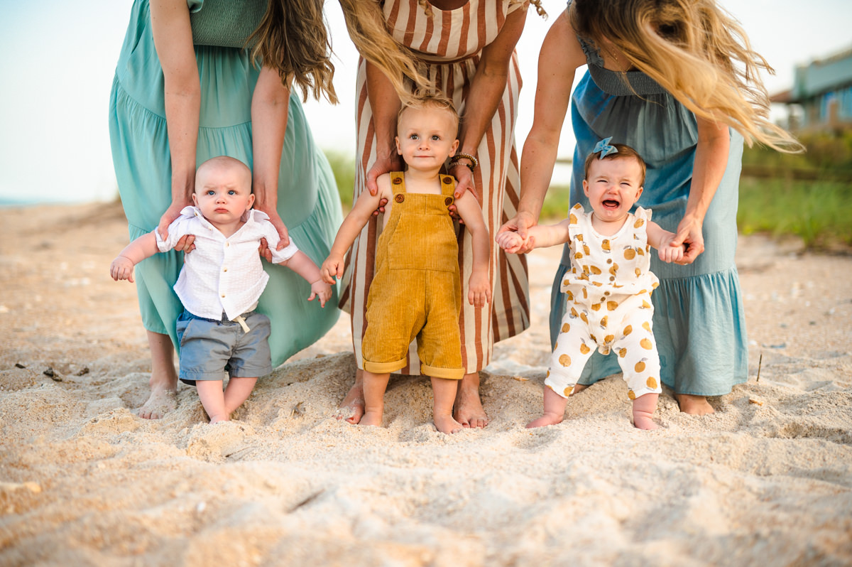 three babies being held in standing positions by their mothers on a beach Jacksonville children's photoshoot