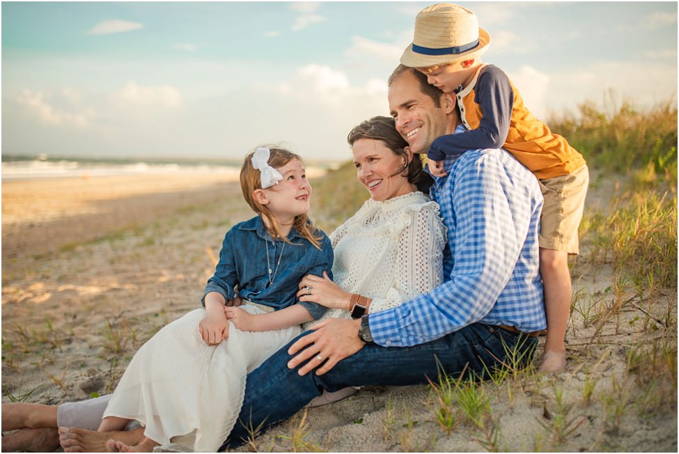 Family smiling with small children sitting on the beach in a family photoshoot in Jacksonville FL