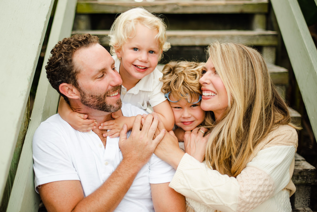 Parents and two small children sitting on steps laughing in a family photoshoot in Jacksonville FL