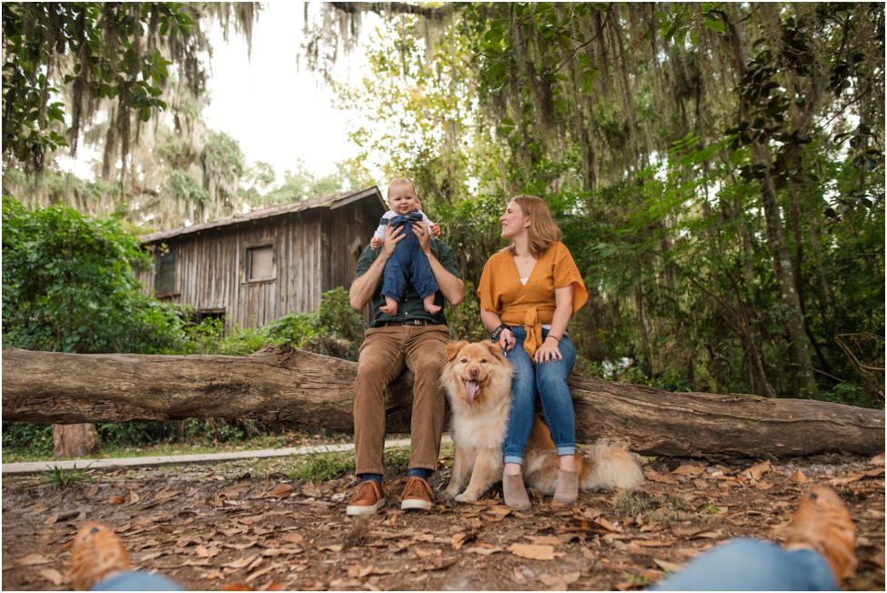 Parents, baby, and dog posing for family photo on a tree trunk in a family photoshoot in Jacksonville FL