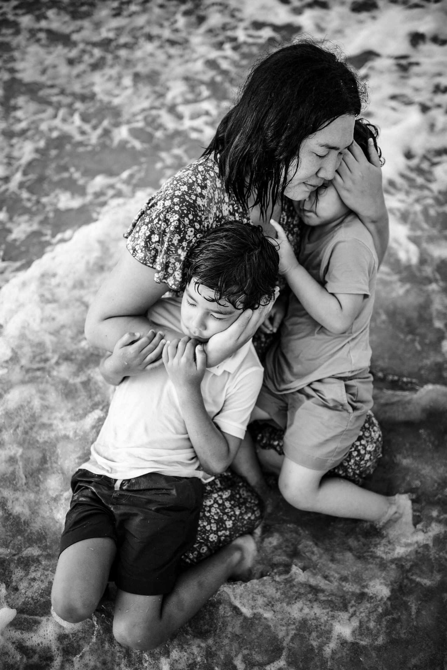 Mother holding her two children on the beach shore in a family photoshoot in Jacksonville FL