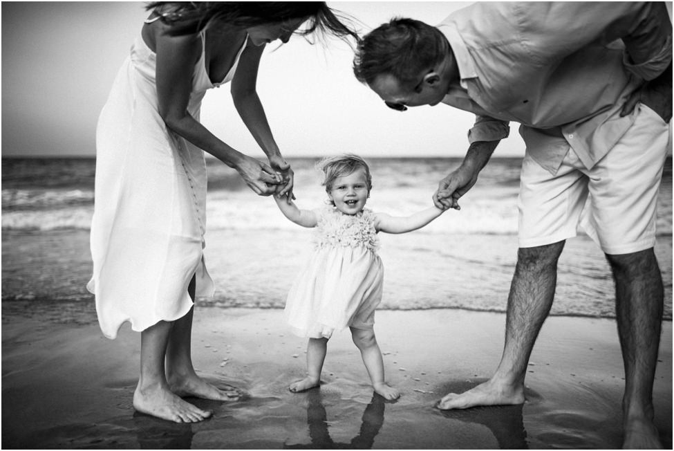 Parents holding toddler's hand on the beach in a family photoshoot in Jacksonville FL