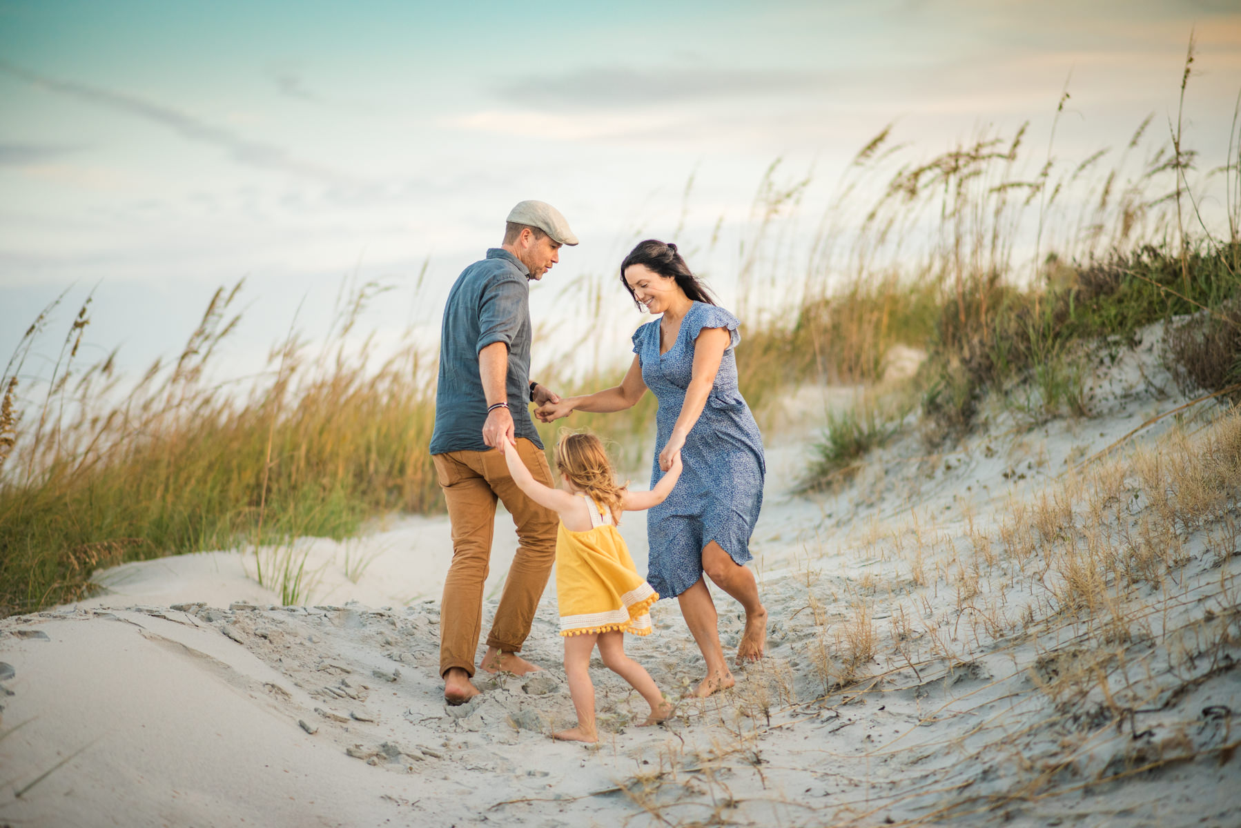Parents and child holding hands laughing and playing on the beach in a family photoshoot in Jacksonville FL