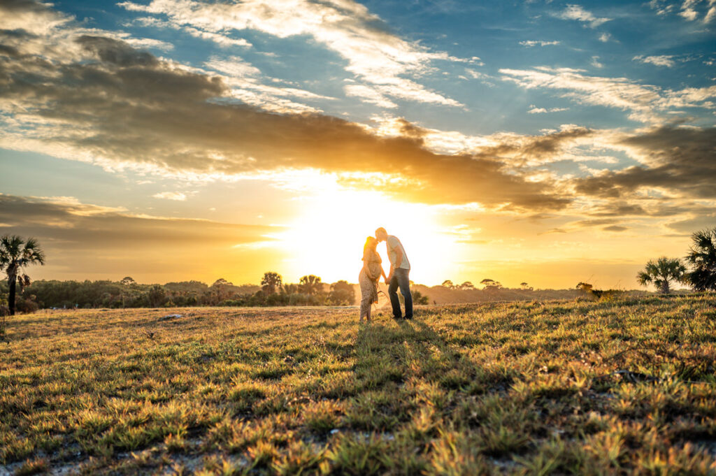 Pregnant couple posing for photos in front of a sunset in a maternity photoshoot in Jacksonville FL