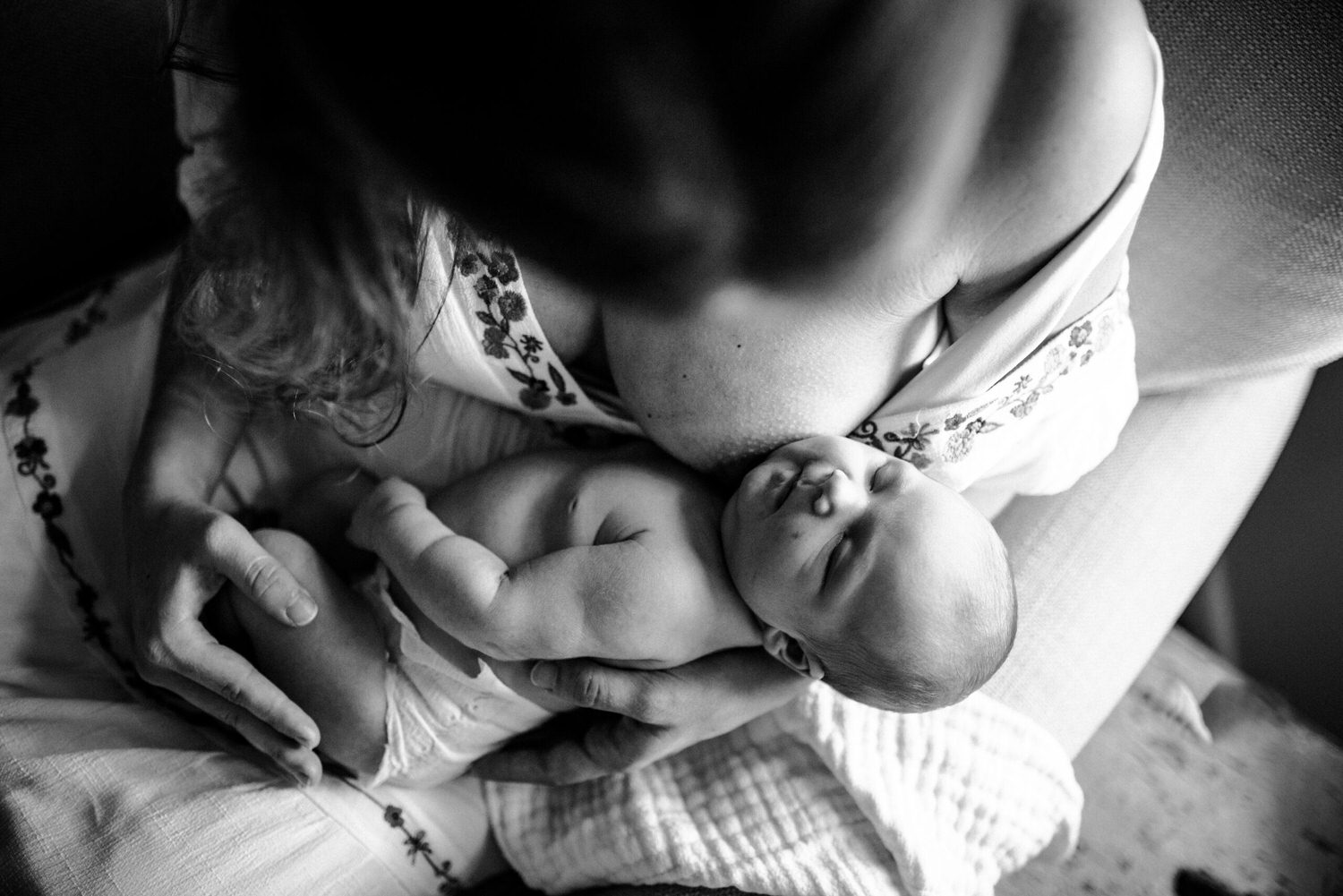 “Black and white photo of a mother cradling her sleeping newborn on her chest, captured from above in a cozy armchair”