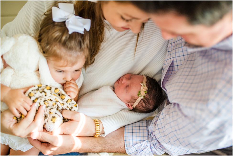 “Parents holding newborn swaddled in a floral headband, big sister with stuffed bunny snuggles close during an intimate lifestyle session in Jacksonville, Florida”
