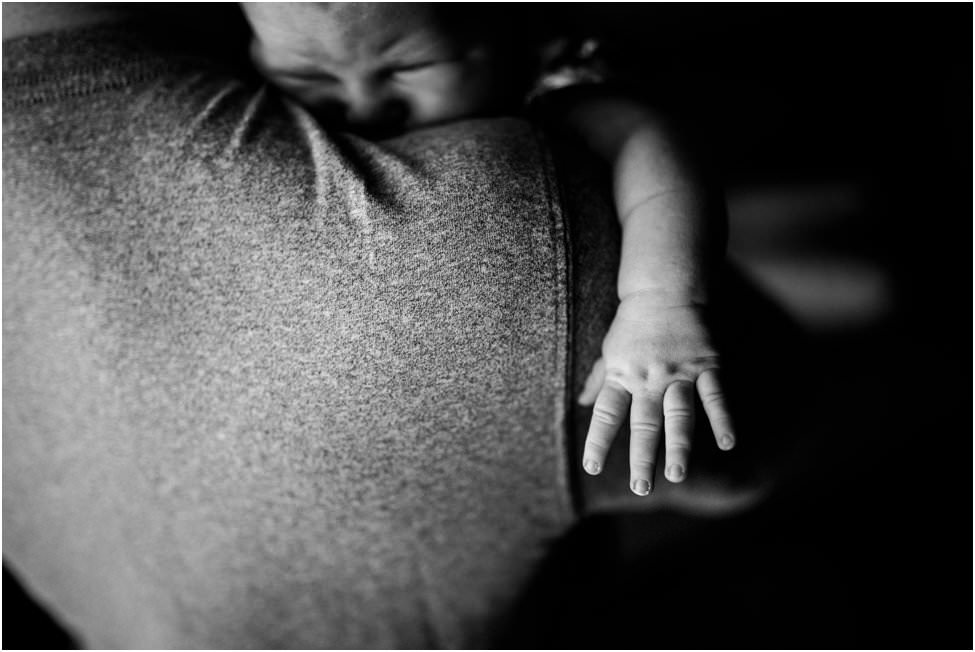 “Close-up of a baby resting on dad’s shoulder with tiny hand reaching outward, captured during an in-home newborn session in Jacksonville by Monika Colichio Photography”