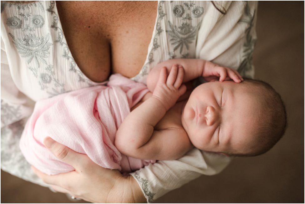 “Newborn baby wrapped in a soft pink blanket sleeping peacefully in mother’s arms, close-up lifestyle photo highlighting delicate features and tender connection.”