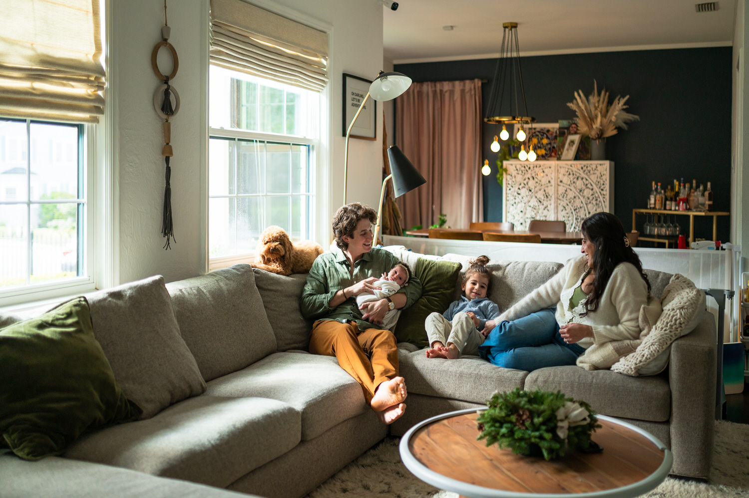 “Family relaxing together on a sectional sofa with their newborn baby, older child, and dog during an in-home lifestyle session in Jacksonville by Monika Colichio Photography”