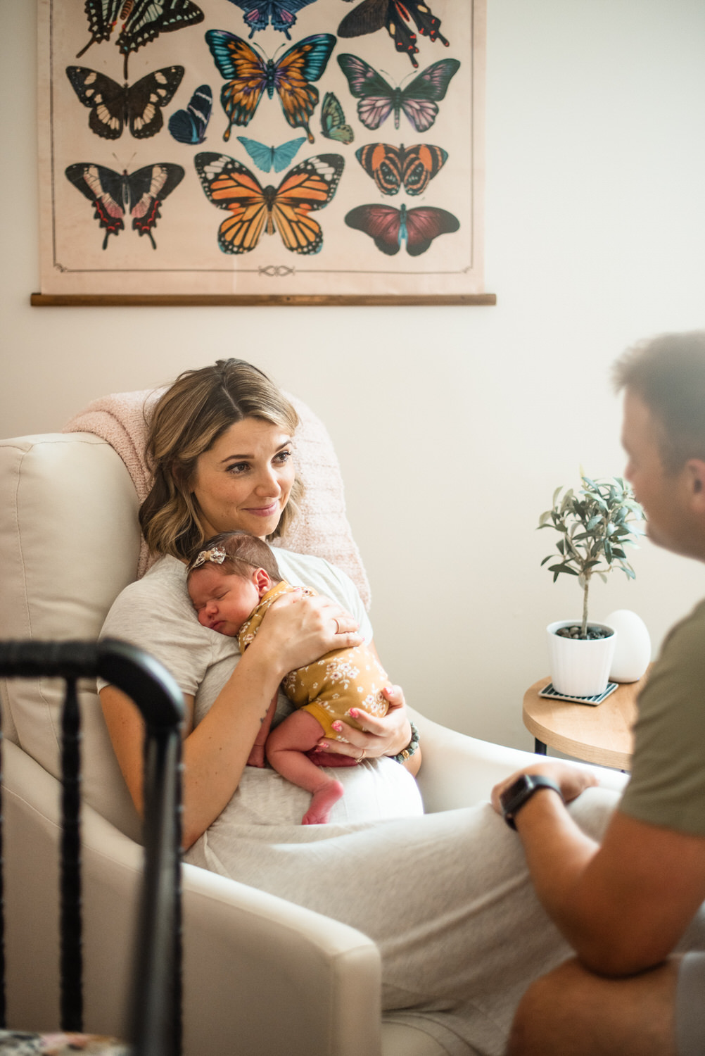 “Mother holding her newborn baby against her chest in a cozy nursery with butterfly artwork during an in-home lifestyle session in Jacksonville by Monika Colichio Photography”