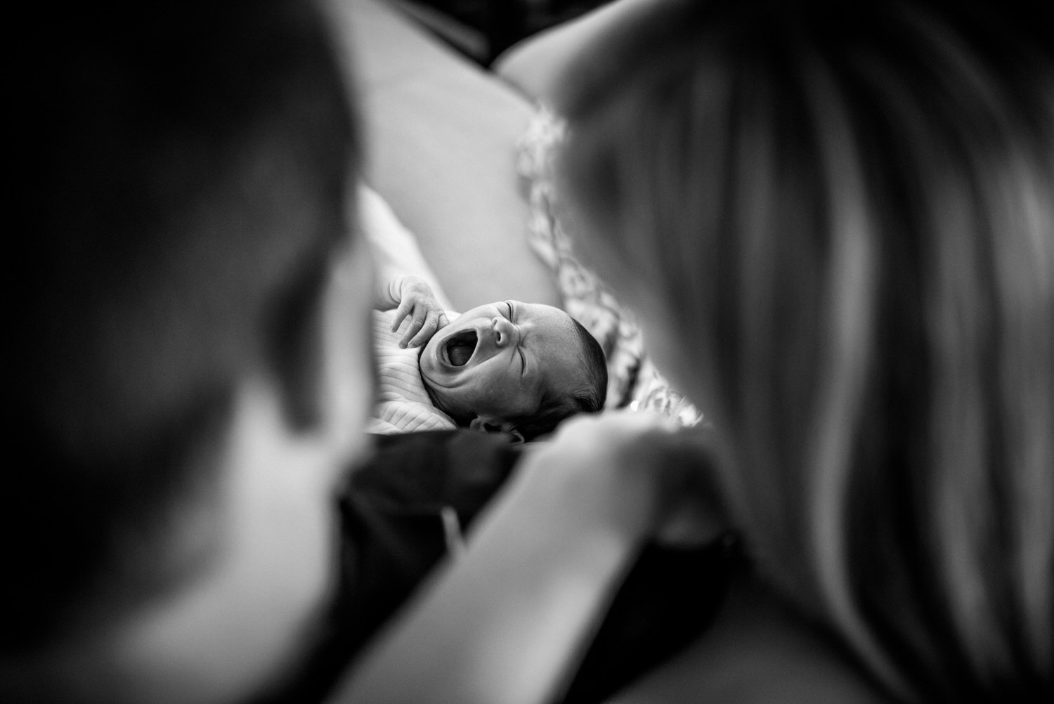“Newborn baby yawning while being held by parents during an intimate in-home lifestyle session in Jacksonville by Monika Colichio Photography”