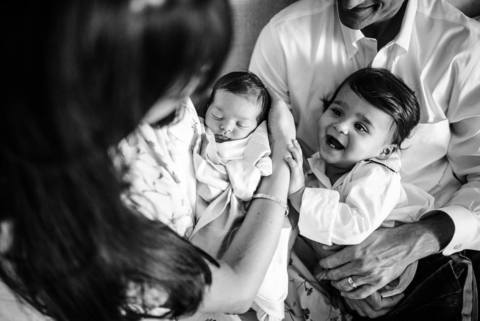 “Family holding their swaddled newborn baby and smiling older sibling during an in-home lifestyle session in Jacksonville by Monika Colichio Photography”