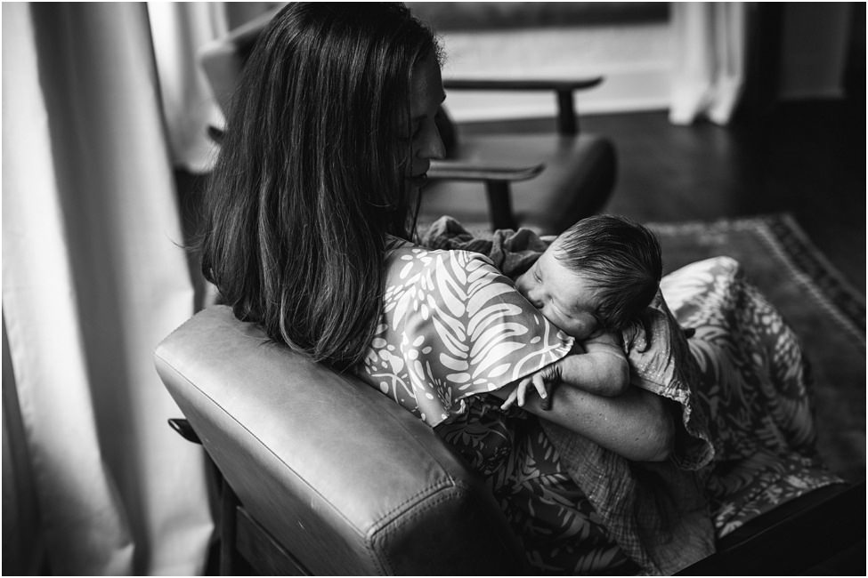 “Mother holding and soothing her newborn baby in a cozy chair during an in-home lifestyle session in Jacksonville by Monika Colichio Photography”