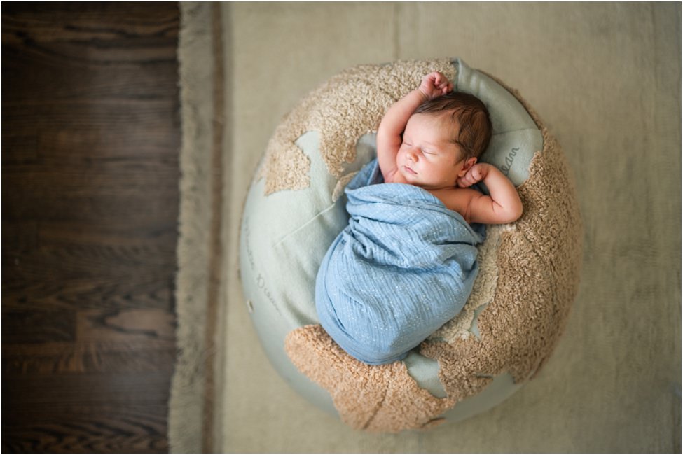 “Newborn baby swaddled in blue, sleeping peacefully on a plush globe-shaped pillow during an in-home lifestyle session in Jacksonville by Monika Colichio Photography”