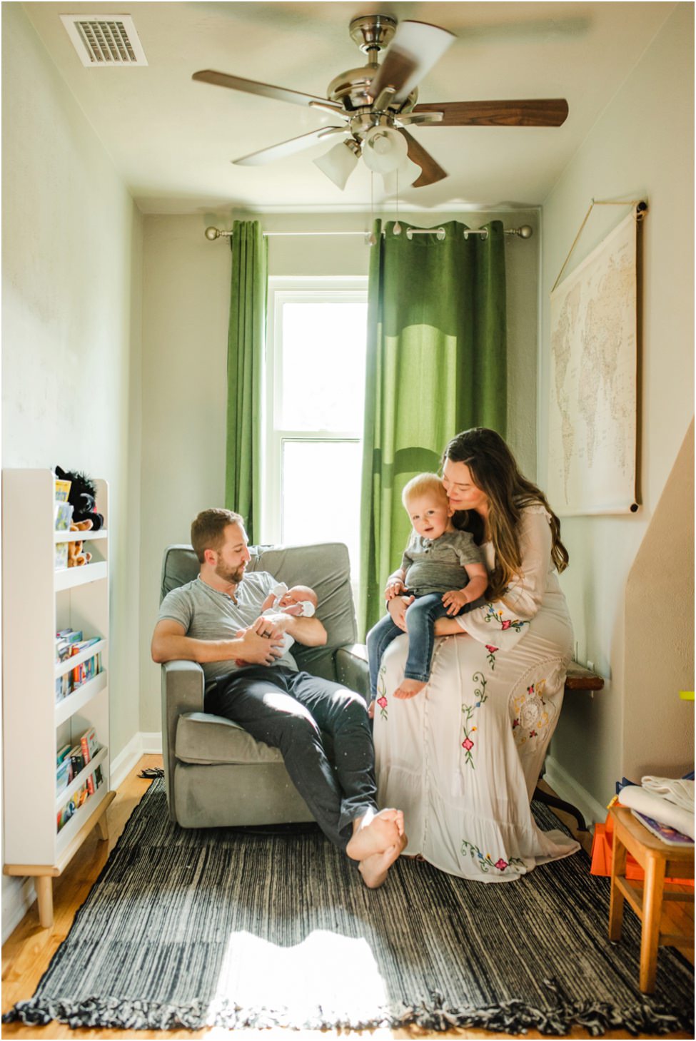 “Family enjoying time together in a sunlit nursery with father holding newborn and mother cuddling toddler during an in-home lifestyle session in Jacksonville by Monika Colichio Photography”