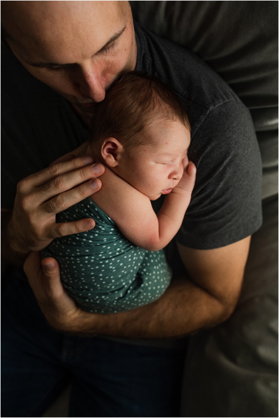 “Father gently holding and kissing his swaddled newborn baby during a cozy in-home lifestyle session in Jacksonville by Monika Colichio Photography”
