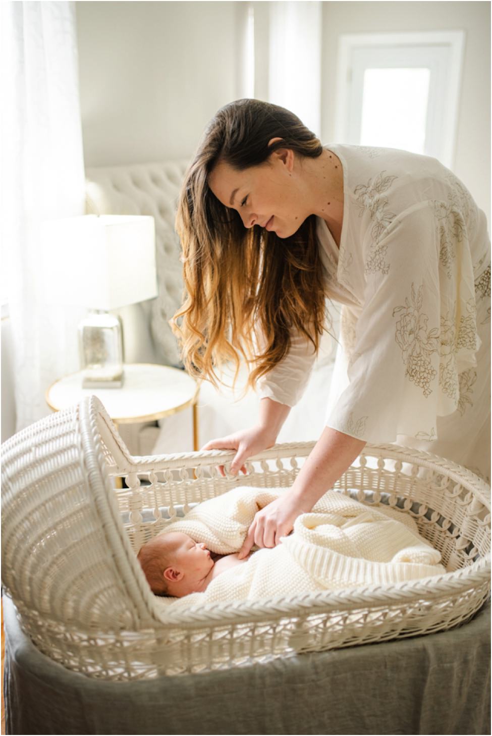 “Mother smiling down at her newborn baby swaddled in a cozy knit blanket in a wicker bassinet during an in-home lifestyle session in Jacksonville by Monika Colichio Photography”
