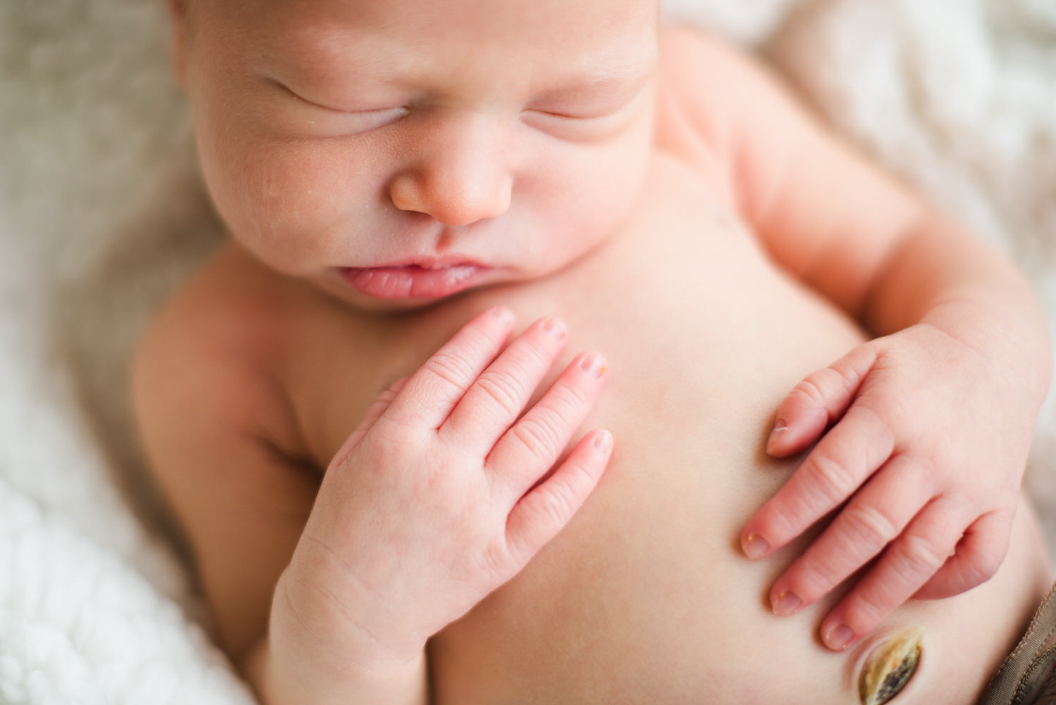 “Close-up of a sleeping newborn baby with eyes closed, tiny hands resting gently on their chest and stomach, showing delicate fingers and healing umbilical cord stump.”