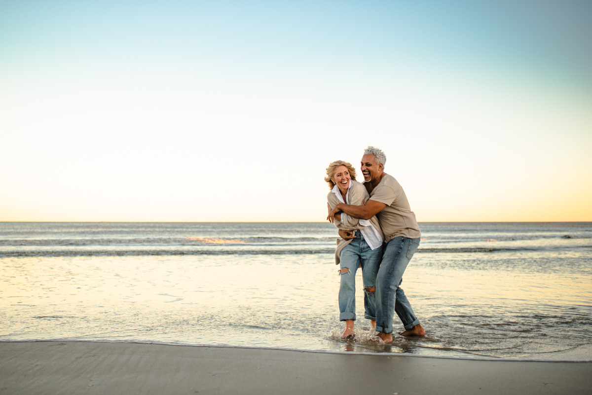 elder couple laughing and playing on the beach shore in a jacksonville couples photoshoot
