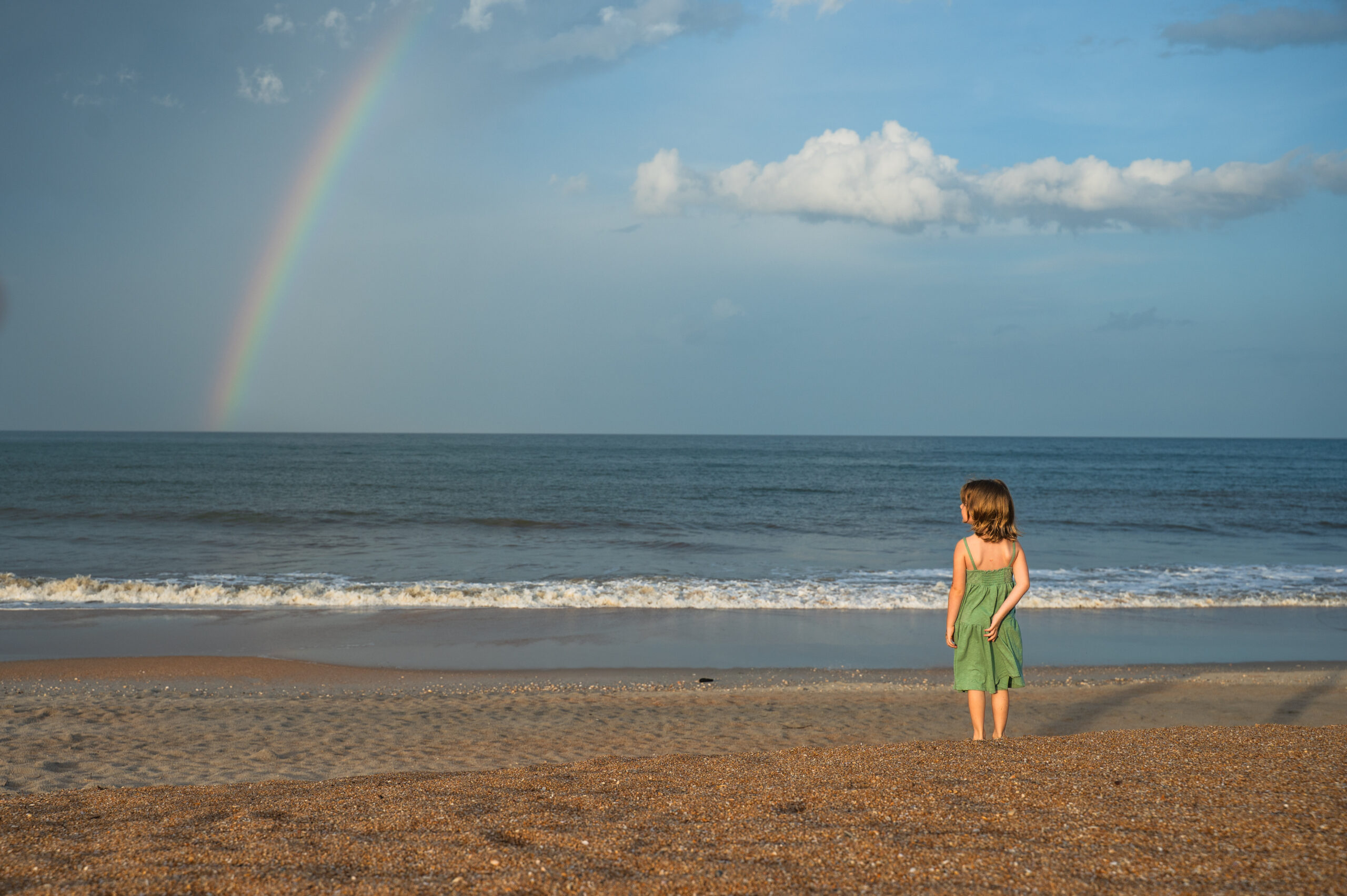 wide angle photo showcasing a young girl on the Ponte Vedra beach standing peacefully under the rainbow by Ponte Vedra family photographer