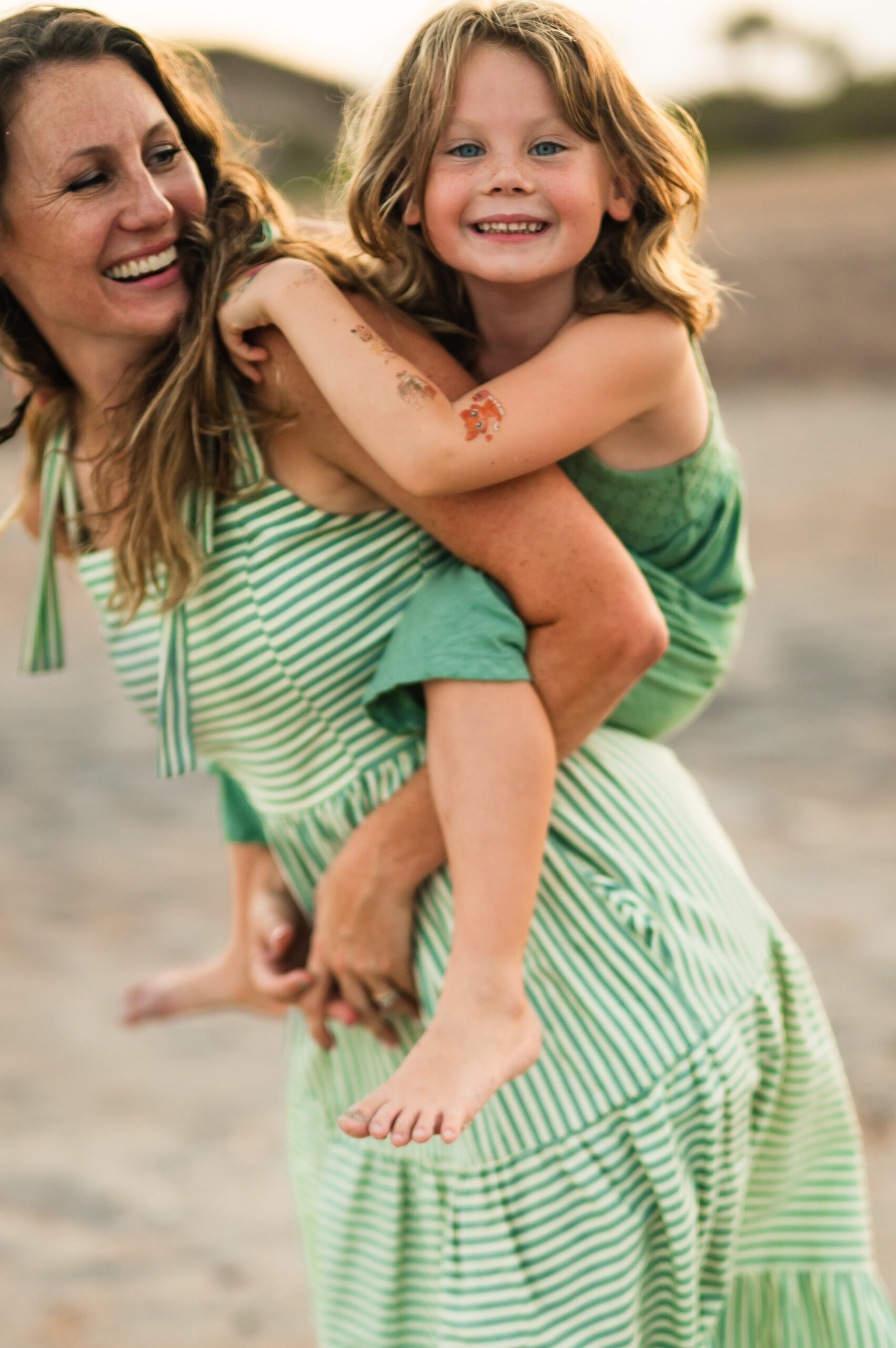 Motherhood portrait of momma and young daughter piggyback on her back and both laughing while at Ponte Vedra Beach