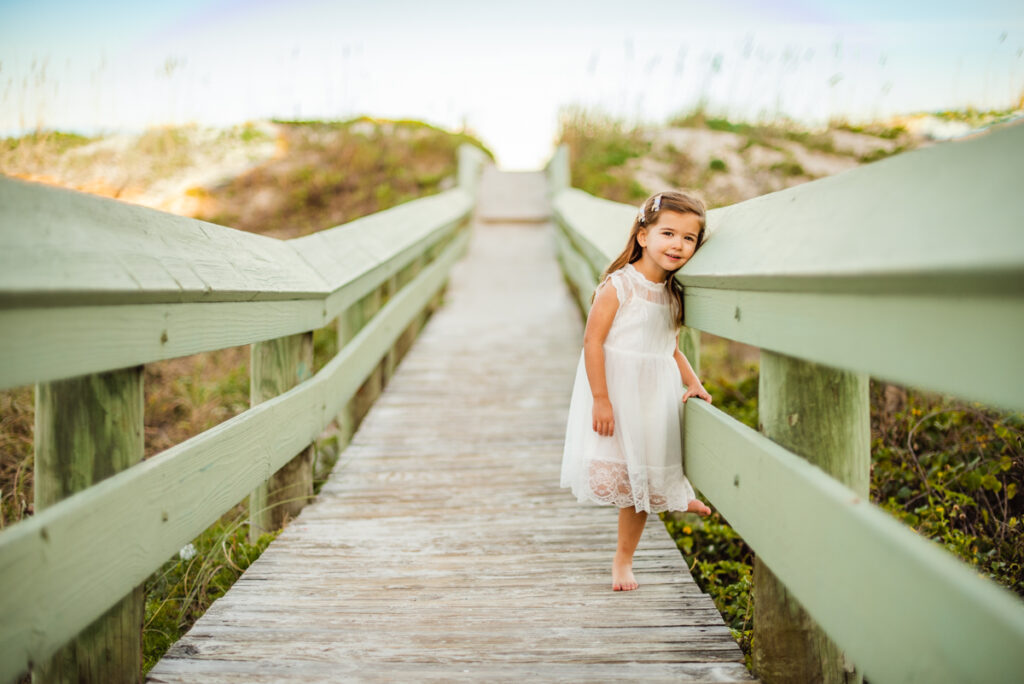 a young girl standing in the beach wooden pathway frames by wooden green rails on the both sides