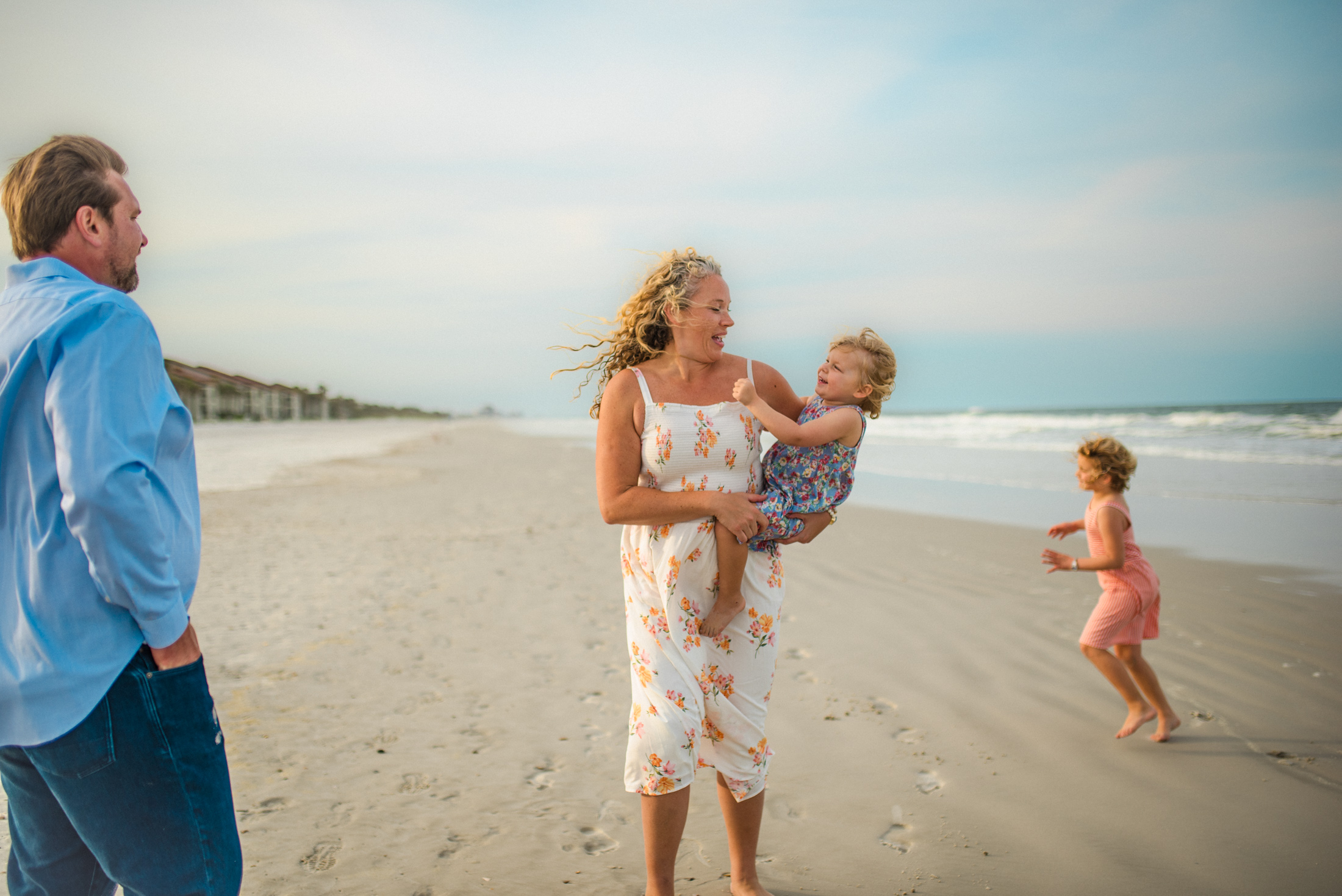 Children playing on the beach with parents hugging in the background in a family photoshoot in Jacksonville FL