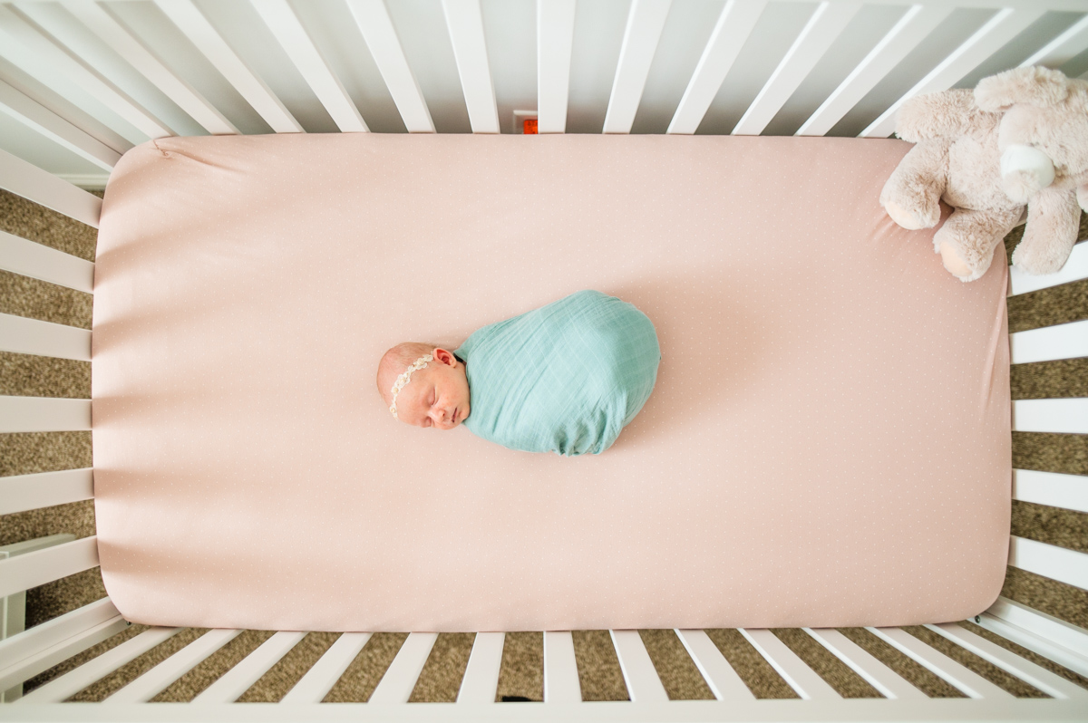 Precious baby girl wrapped in the aqua wrap and wearing a headband laying in the crib while peacefully sleeping