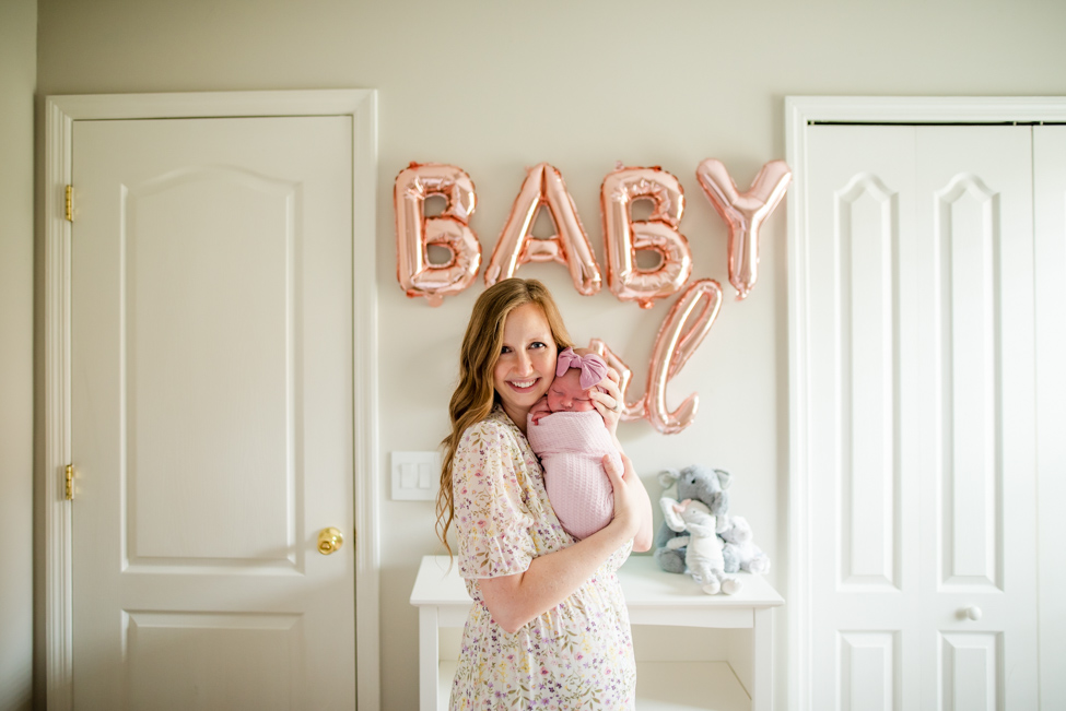 momma holding her precious baby girl in the background of cute nursery decorated by balloons