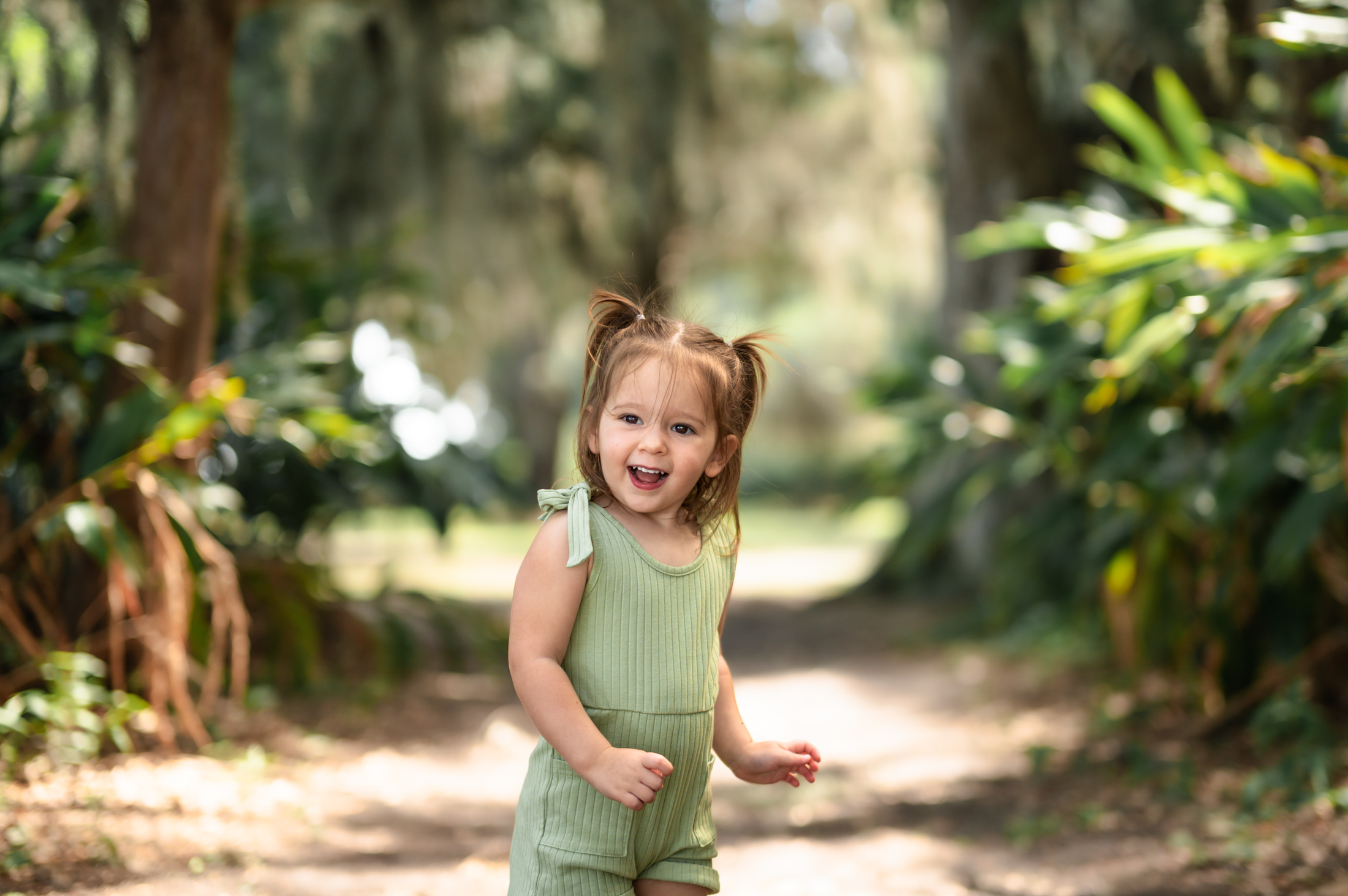 Giggling young girl with ponytails wiggling and jumping during outdoor Jacksonville family session in the park