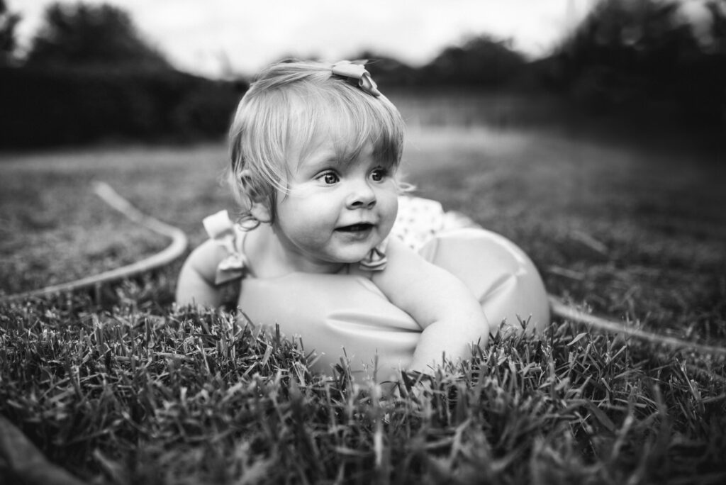 Joyful black and white portrait of a smiling baby girl lying on the grass, captured outdoors by a Jacksonville children photographer