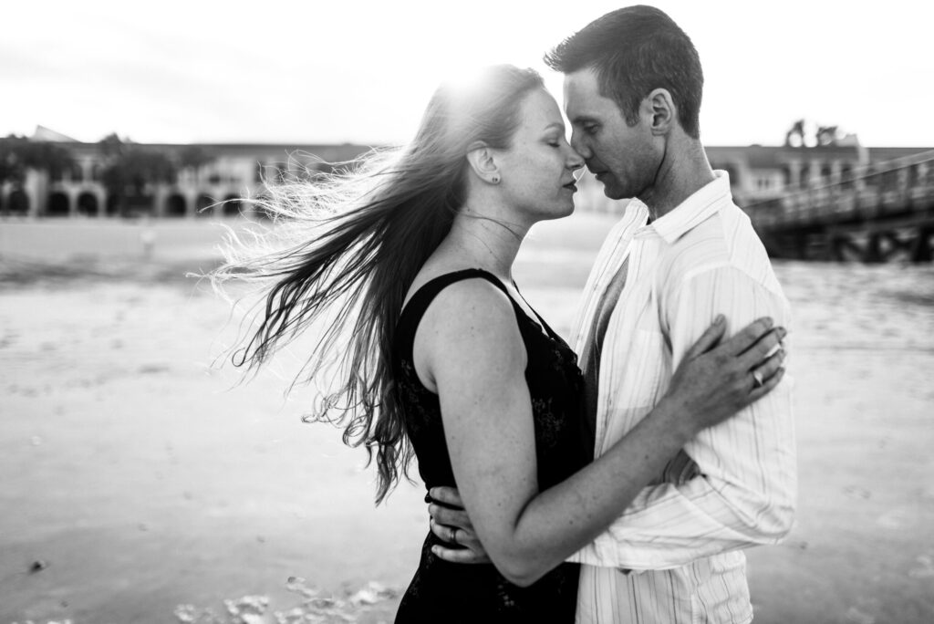 Emotive beach portrait of parents embracing each other during beach family session with mom's hair swept by the wind