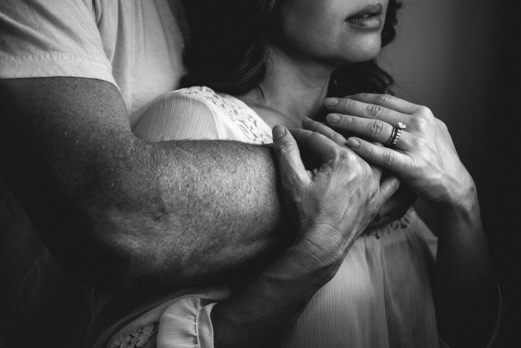 Emotive black and white portrait of a couple embracing, highlighting intimate hands and engagement ring — captured by a Jacksonville photographer
