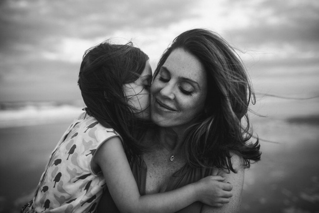 Emotive black and white portrait of mom and daughter in the windy evening hugging each other and daughter kissing momma — captured by a Jacksonville photographe