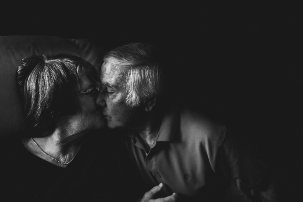 Heartwarming black and white portrait of a elderly couple kissing in their home, captured by a Jacksonville family photographer